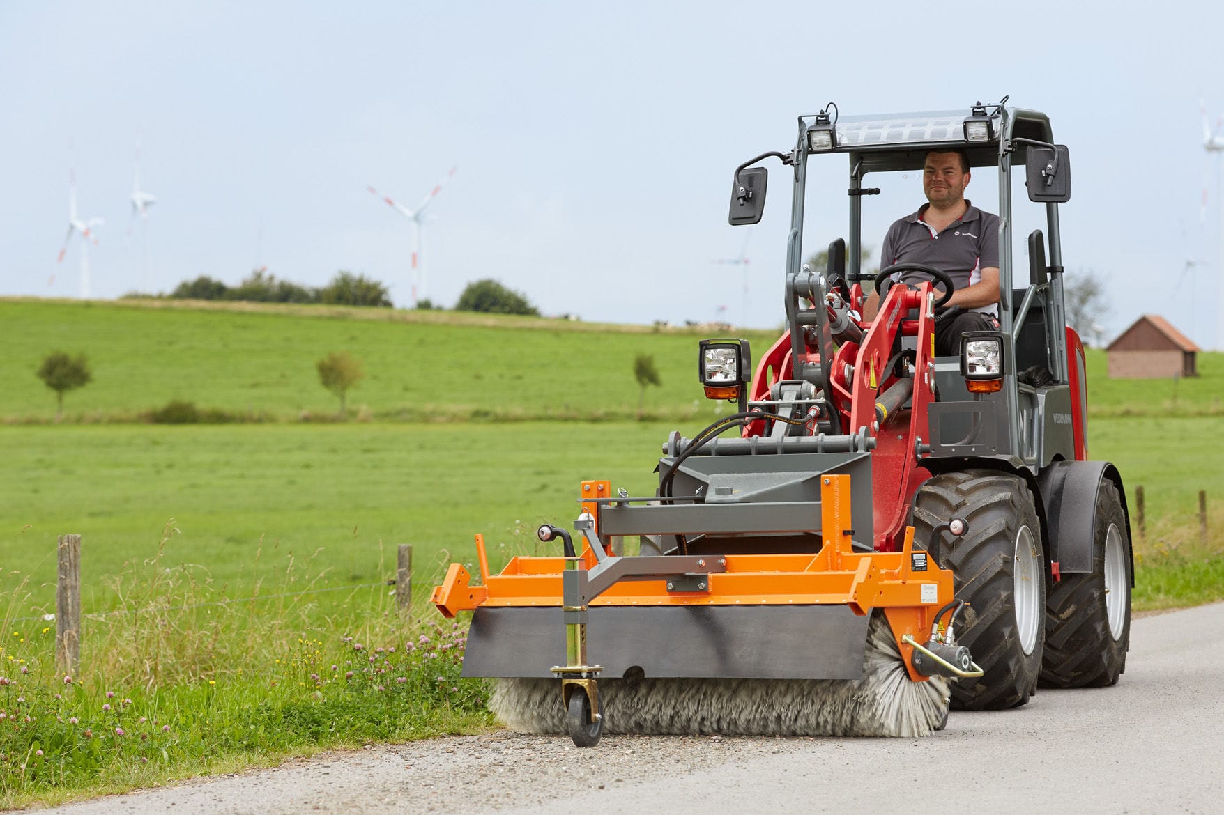 Radlader mit Kehrmaschine bei der Reinigung eines Weges